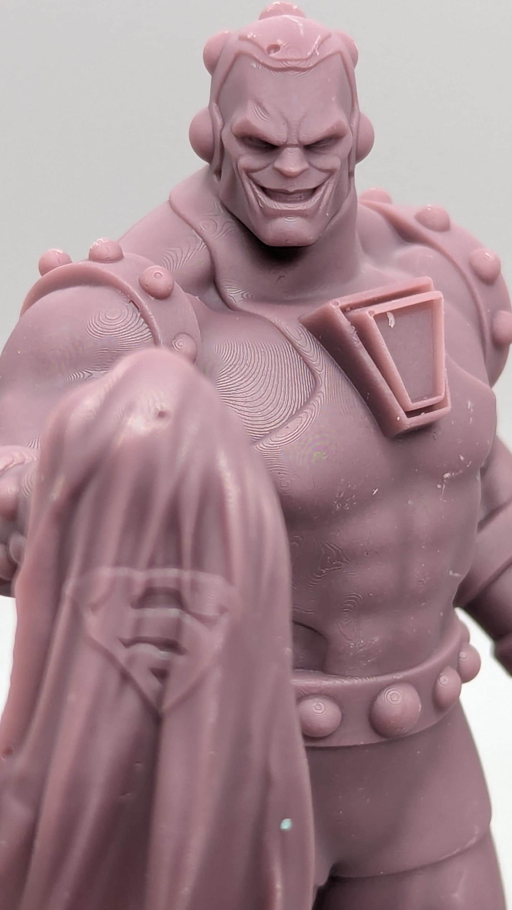 A close-up image of a pink plastic figurine depicting a muscular superhero character with a determined expression.