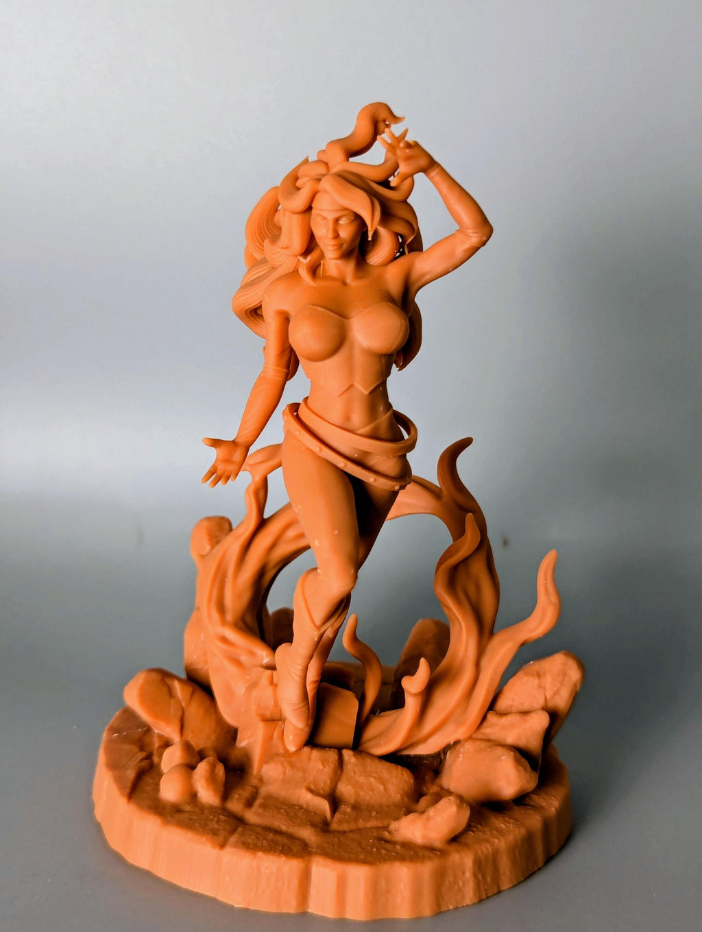 a figurine of a woman with long hair, standing on a rock formation with flames or fire behind her.