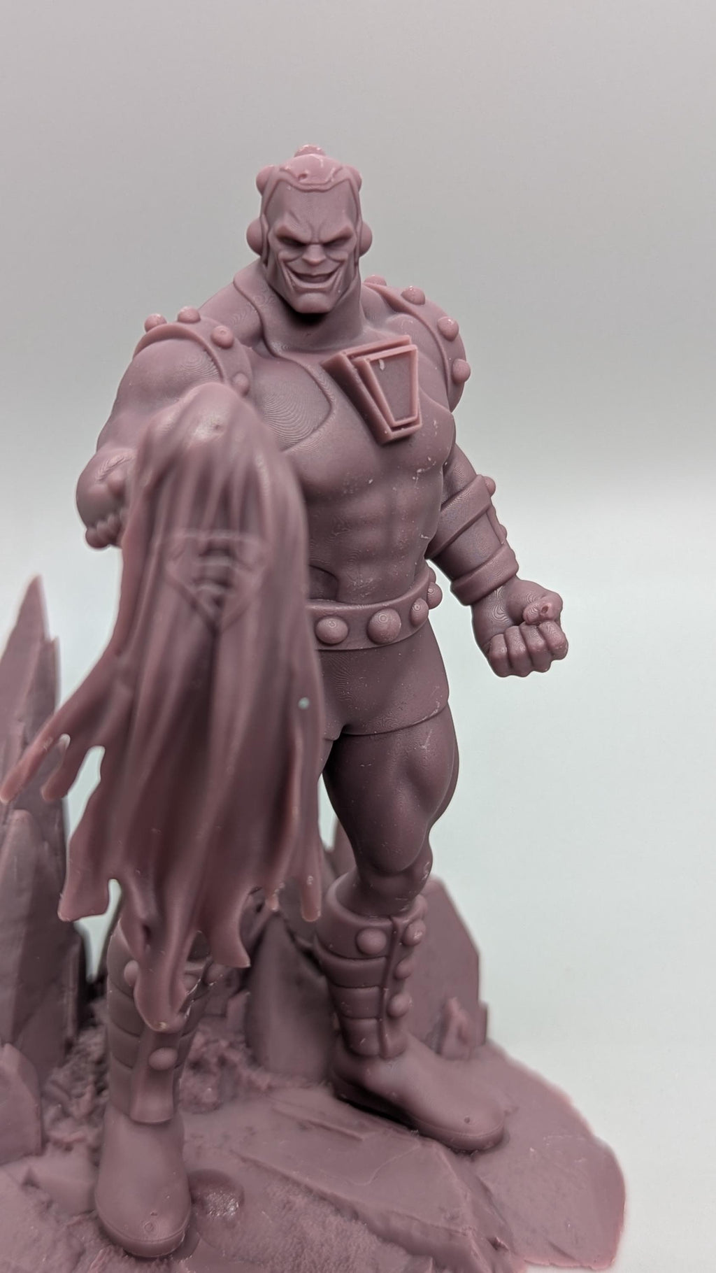 A figurine of a muscular, armored character with a cape-like design on the back, standing on a rocky surface.