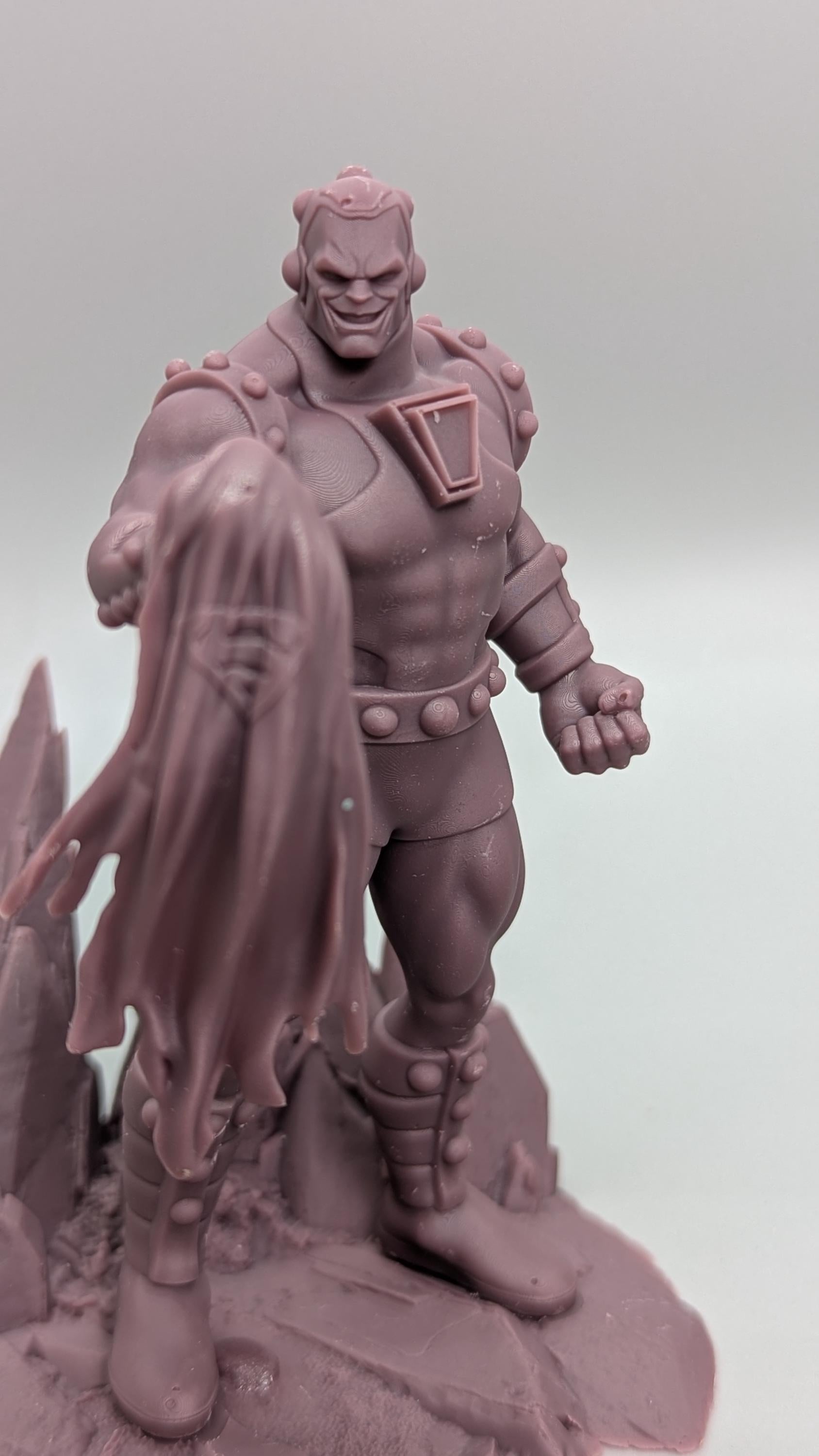 A figurine of a muscular, armored character with a cape-like design on the back, standing on a rocky surface.
