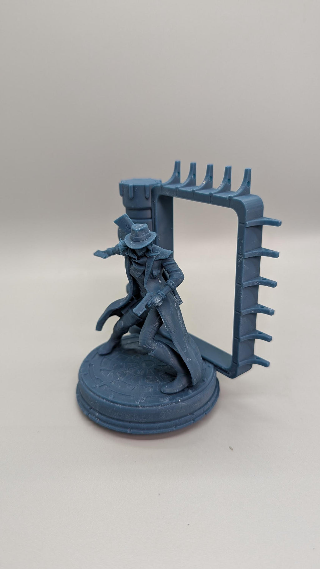 A figurine of a person in a hat and coat, standing on a platform with a rectangular frame attached to it.