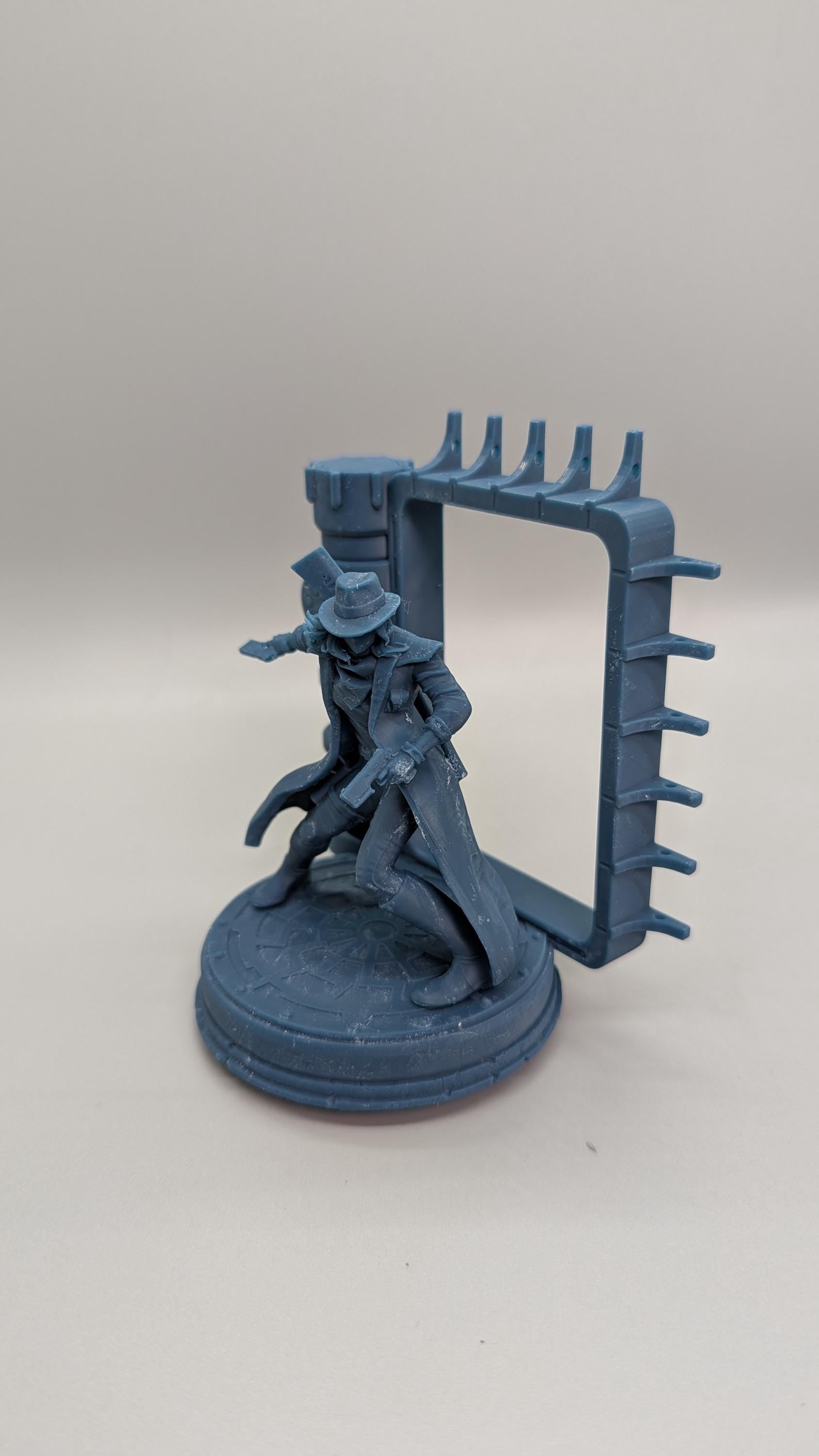 A figurine of a person in a hat and coat, standing on a platform with a rectangular frame attached to it.