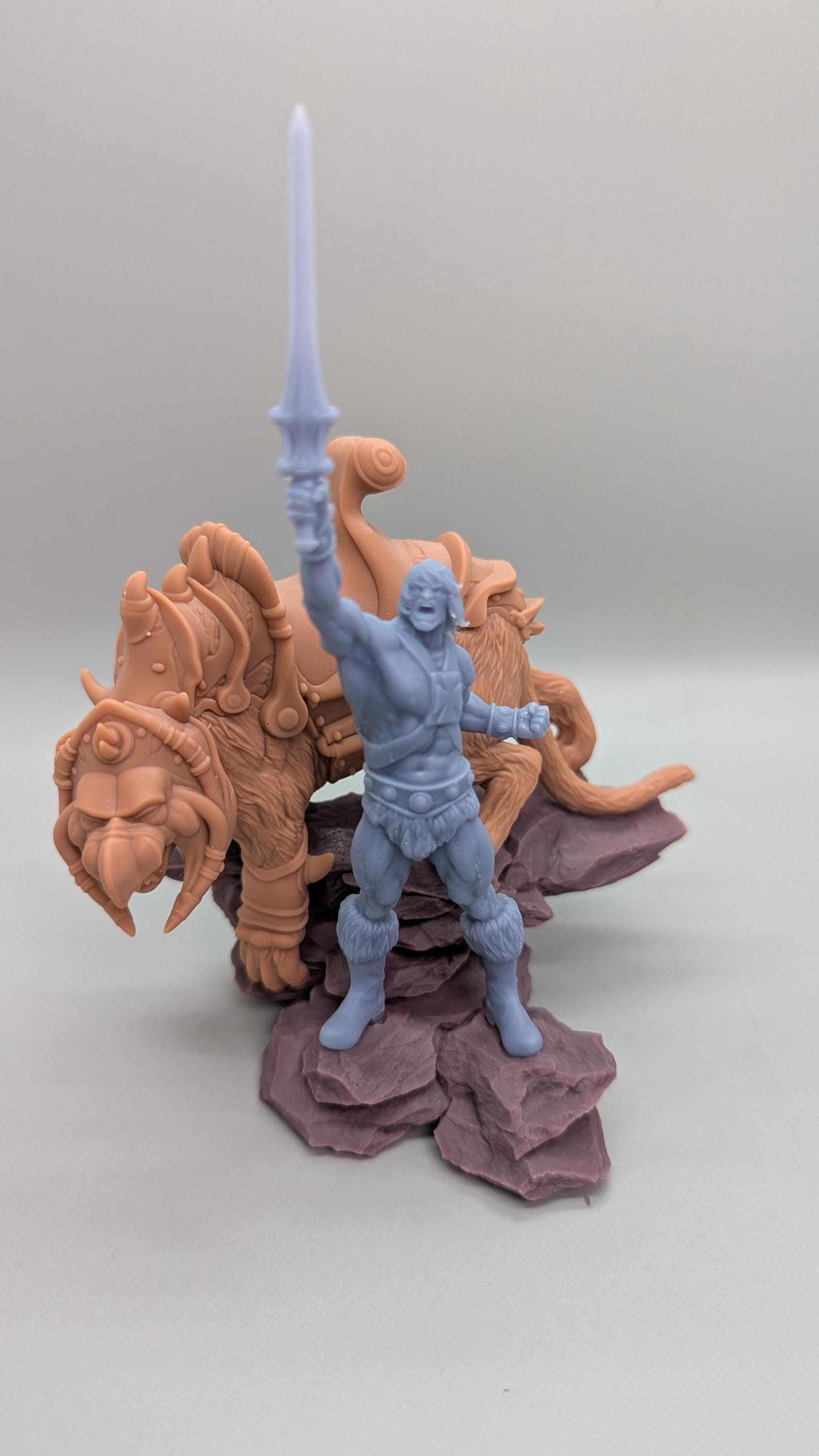 A figurine of a muscular man holding a sword stands on a rock formation, with a large, fierce-looking creature, possibly a dragon or a lion, behind him.