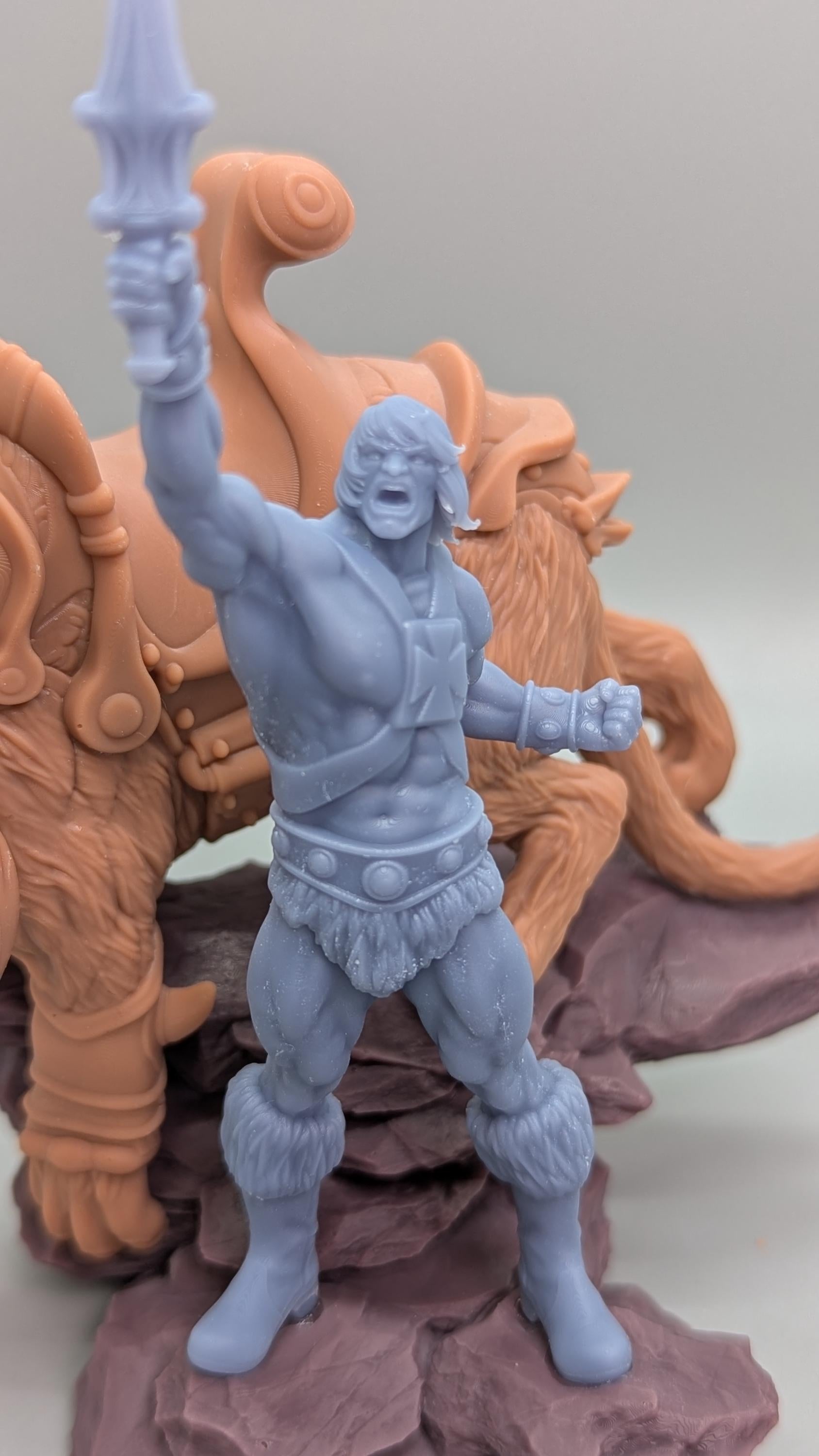 A toy figurine of a muscular man with a sword, standing on a rock formation.