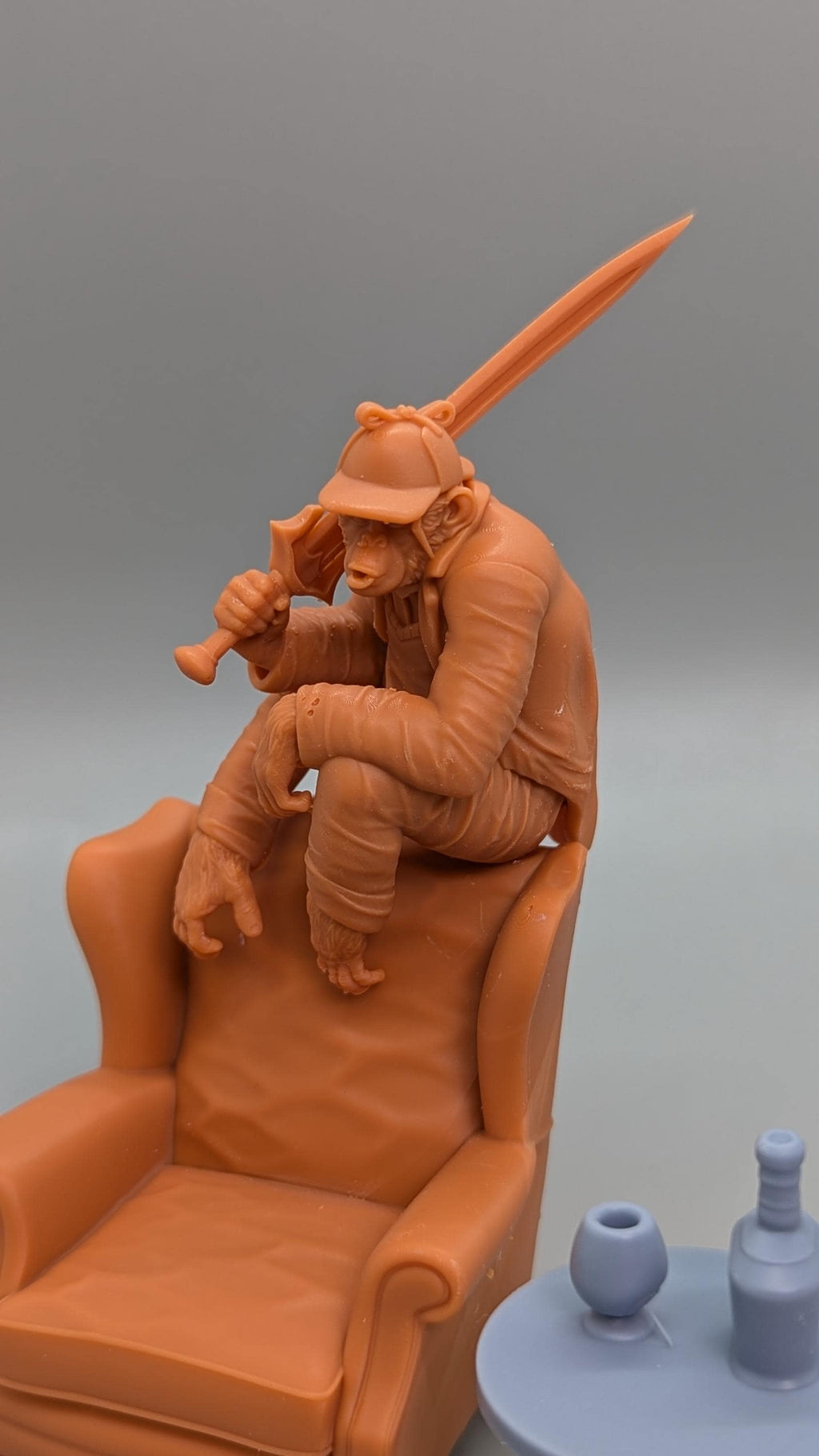 A figurine of a monkey sitting on a chair, holding a sword in its hand.