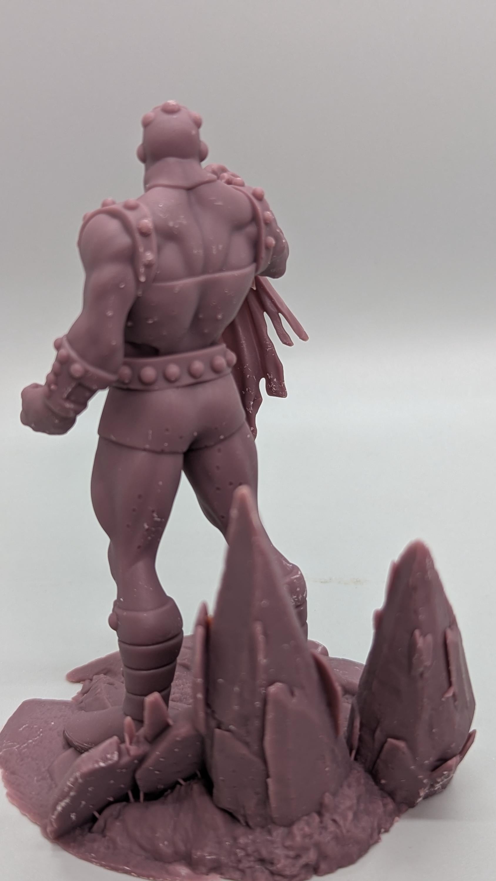 A figurine of a muscular, armored figure standing on a rocky base.