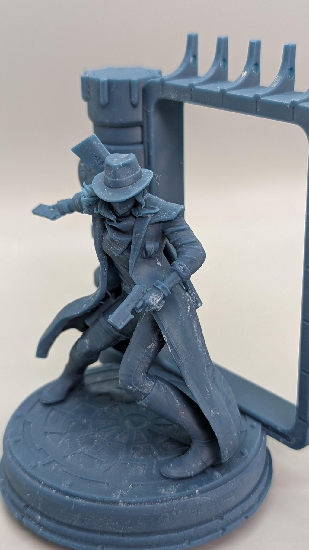 A figurine of a person in a hat and coat, holding a gun, standing on a platform with a decorative border.