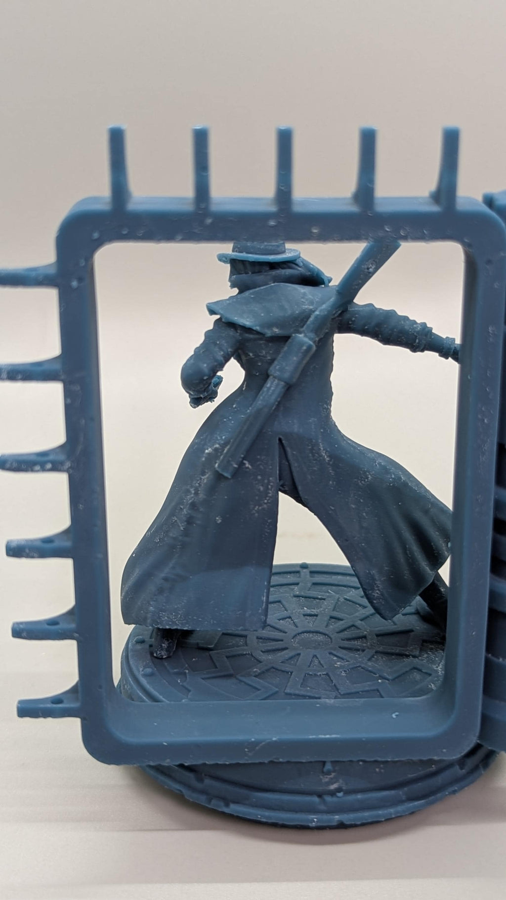 A dark blue figurine of a person in a long coat and hat, holding a sword, is displayed within a blue plastic frame.