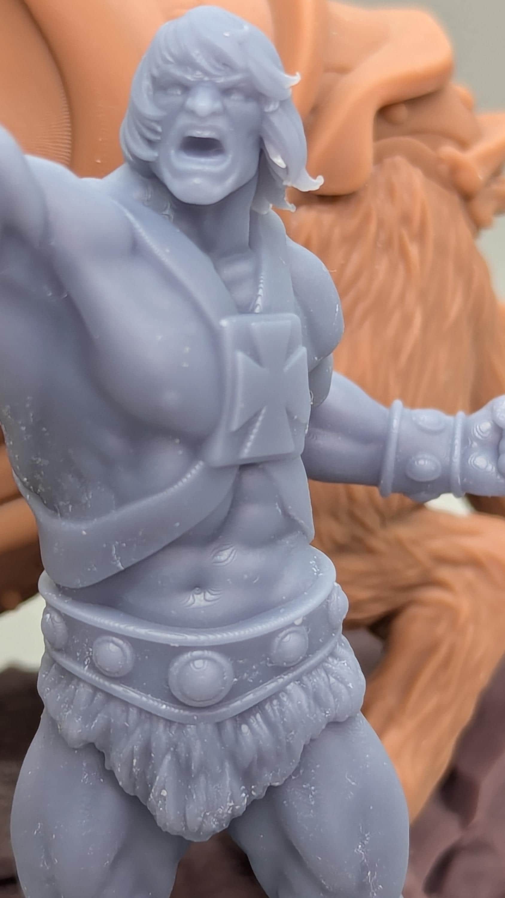 A close-up image of a figurine of a muscular, bearded man with a determined expression, wearing a belt with circular buttons.
