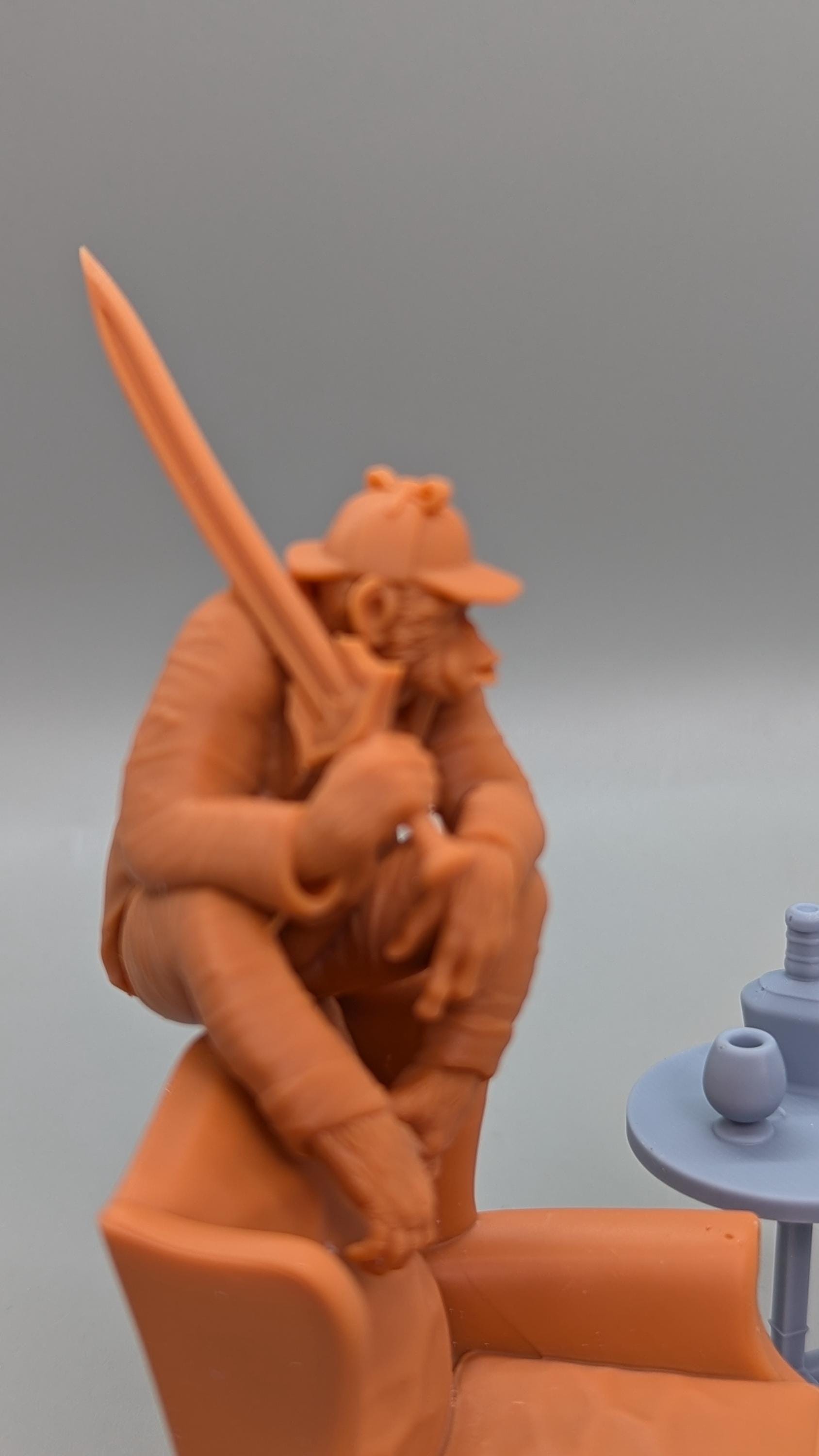 a figurine of a person sitting in a chair, holding a sword in their hand.